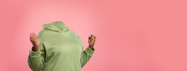 A headless person in a green hoodie exudes excitement with raised fists. The vibrant pink backdrop emphasizes the lively atmosphere and adds a creative touch to the composition.