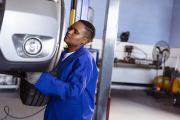 Young adult African American woman mechanic inspecting car bumper and wheel in auto repair garage