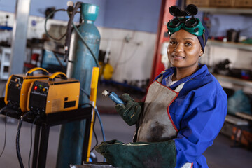 African American woman welder standing with welding torch in fabrication shop, copy space