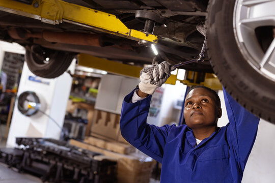 African American woman tightening part under car on lift with socket wrench in garage, copy space