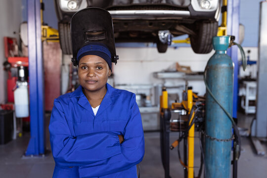African American female standing in garage with welding helmet flipped up near hydraulic lift
