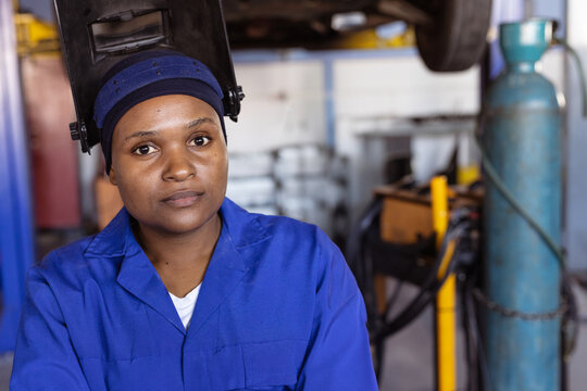 African American woman inspecting automotive workshop, with welding helmet flipped up and tool cart