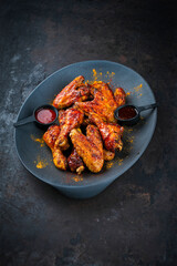 Authentical barbecue chicken wings and drumsticks with hot chili and grill sauce served as close-up on a design plate