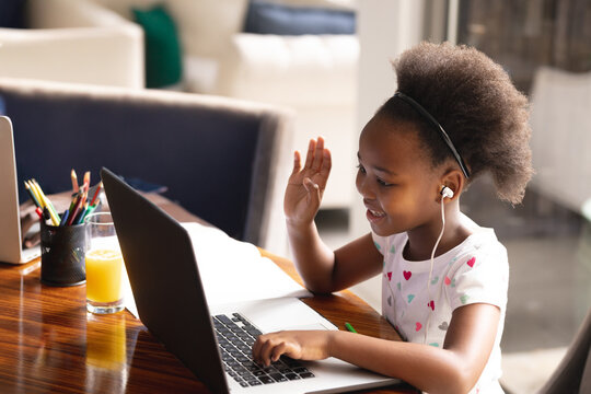 African American girl raising hand while typing on laptop at home with colored pencils, copy space