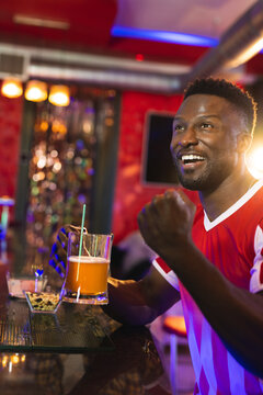 African American man cheering at bar under warm lights, with beer mug, sequin panels, copy space