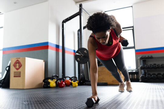 African American woman performing one-arm dumbbell row in gym, with kettlebells, copy space