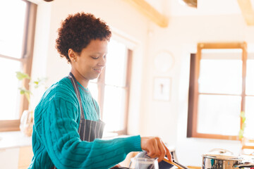 Non-binary person cooking in home kitchen with stainless-steel pot and wooden spoon, copy space