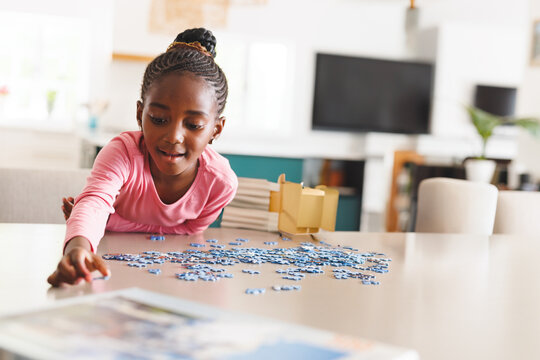 African American girl arranging puzzle pieces on table near wooden box in living room, copy space