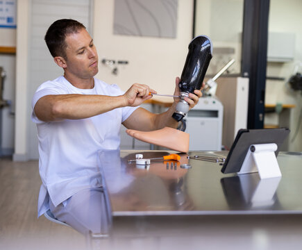 Male prosthetics technician adjusting carbon fiber leg at medical lab bench, with digital tablet