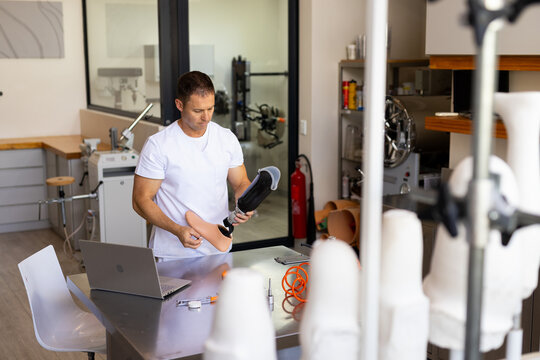 Male technician inspecting below-knee prosthetic leg on workbench in prosthetics workshop