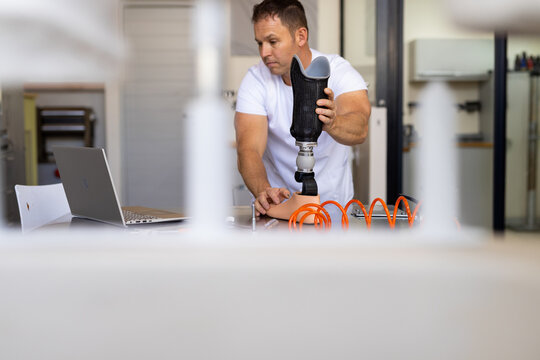 Senior man examining prosthetic socket and pylon in laboratory, with laptop and tubing, copy space
