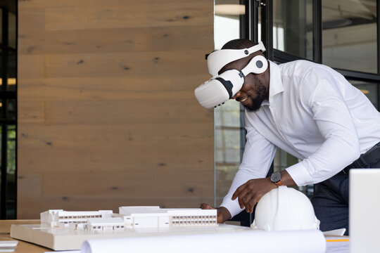 Young adult African American man examining scale model with VR headset in modern office, copy space
