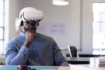 African American man sitting at desk in studio, with VR headset, cutting mat and model pieces