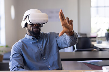 Young adult African American man using virtual reality headset at open office desk, with papers