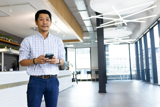 Asian man checking smartphone in modern office lounge, with coffee machine and potted plants