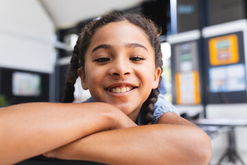 Schoolgirl leaning on desk in classroom, smiling at camera with educational displays