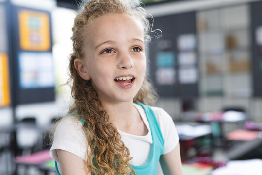 8-year-old girl smiling and talking in class, with desks chairs cabinets and bulletin board posters