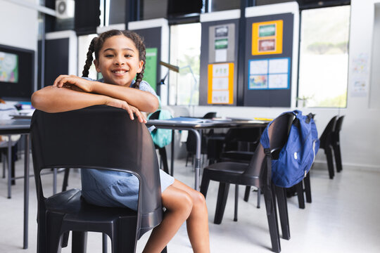 Girl student leaning on black chair back in classroom with blue backpack on desk, copy space