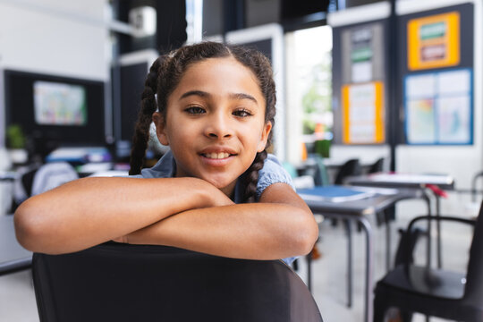 Girl child leaning on chair back among student desks in classroom, showing posters and monitor