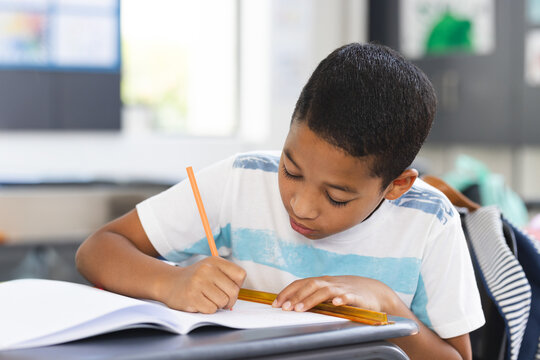 Boy student leaning over notebook working at desk in elementary classroom, using pencil and ruler