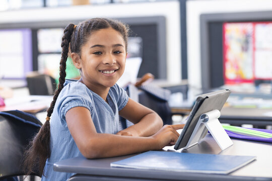 8-year-old girl sitting at school desk using tablet in classroom with notebook and folder