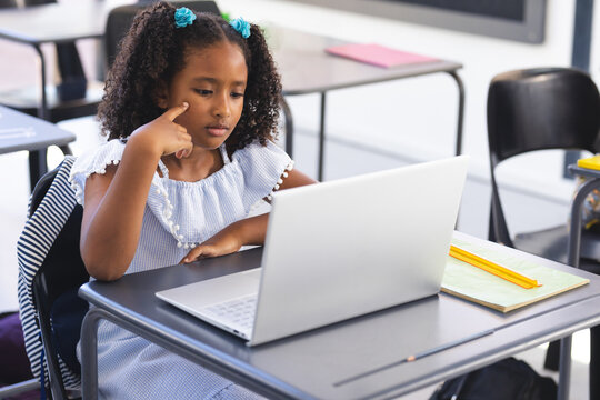 Multiracial child studying on silver laptop at elementary school desk with notebook and pencil