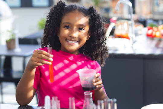 Child performing home kitchen experiment mixing orange liquid in test tube and using measuring cup