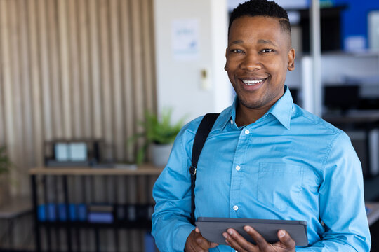 African American woman holding tablet in office reception, with binders and plant, copy space