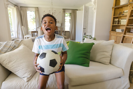 African American boy holding soccer ball in living room, showing playful energy and excitement