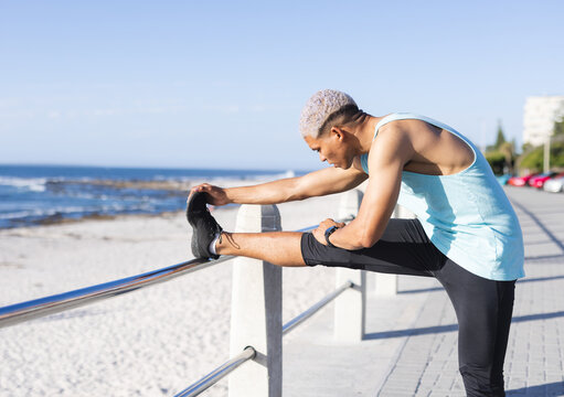 man stretching leg on metal railing at beachside promenade, with shoes and smartwatch, copy space