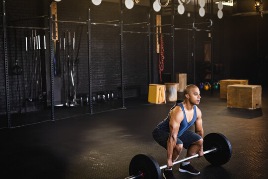Man lifting loaded barbell in industrial gym, with metal rig, gymnastic rings and kettlebells