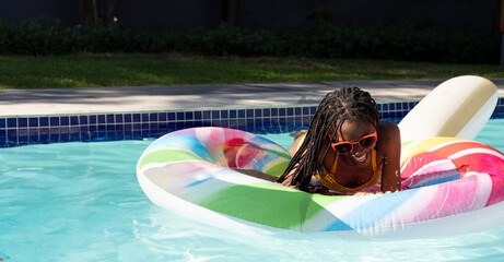 African American teenage girl floating on inflatable pool ring in backyard pool, wearing sunglasses