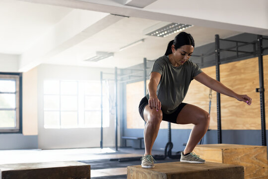 Woman performing box jump squat on plyometric box in industrial gym with metal rig, copy space
