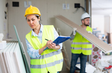 Strict focused asian female building inspector wearing yellow safety vest and hard hat standing...