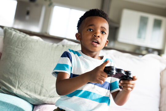 African American child playing video game on couch in living room, holding black controller