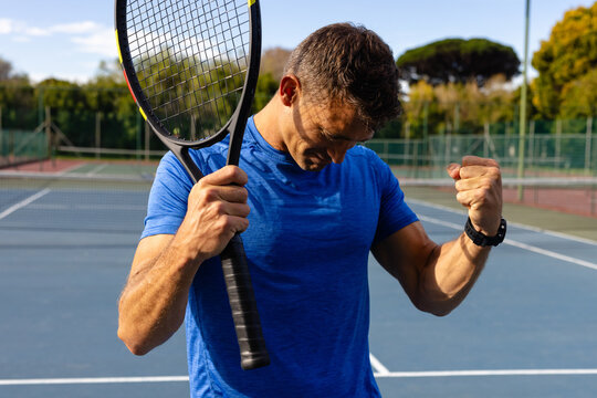 Mid-adult man celebrating winning point on outdoor tennis court, with tennis racket and smartwatch