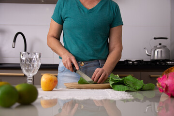 Mulher de 50 anos cortando couve para fazer suco verde detox