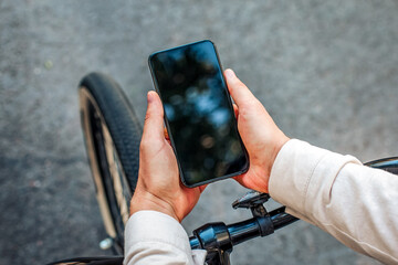 Social networks in city outdoors. Guy sitting on bike and looking at smartphone with blank screen, top view