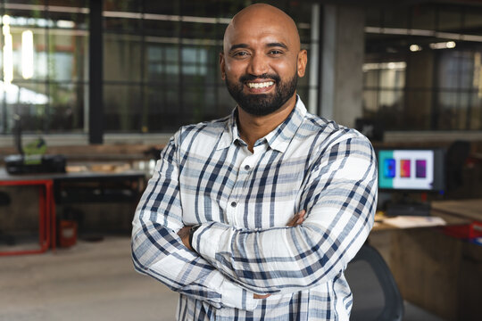 Mid-adult man standing smiling in industrial studio, showing workbench tools and computer monitor - Powered by Adobe