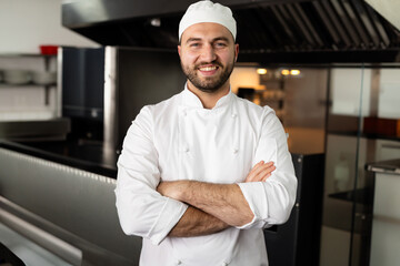 Male chef wearing jacket and standing in commercial kitchen, showcasing ventilation hood and ovens