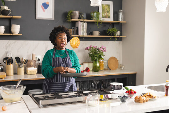 African American woman flipping pancake in modern home kitchen, with frying pan and mixing bowl