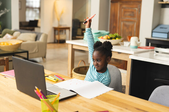 African American girl sitting in modern home, holding pink marker with colored pencils, copy space