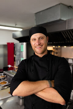 Male chef standing with arms crossed in restaurant kitchen, showing plated food on steel counter