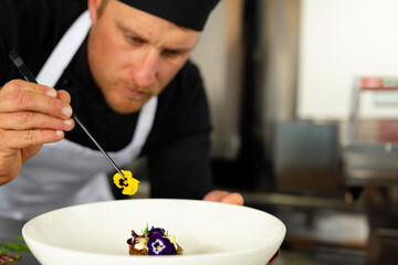 Mid-adult male chef placing yellow flower on dish using tweezers in restaurant kitchen, copy space