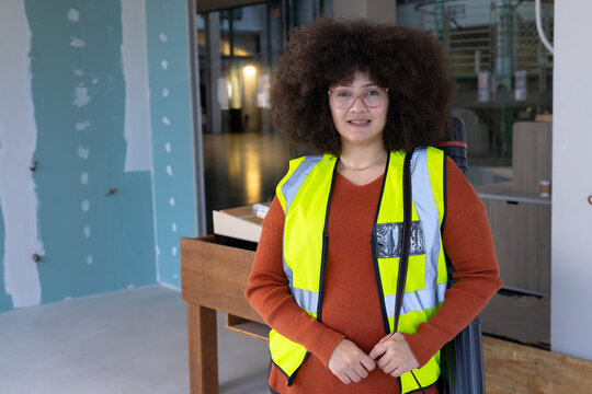 Mid adult woman inspecting office construction site, wearing safety vest and carrying blueprint