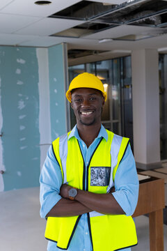 African American man smiling and standing in building site, wearing yellow hard hat, vest, watch