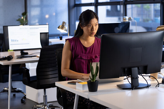 Asian woman working on computer at open-plan office, with laptop keyboard mouse and succulent plant