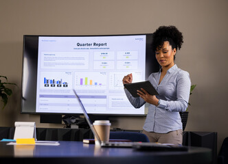 Businesswoman presenting quarterly report on wall display in meeting room with tablet, copy space