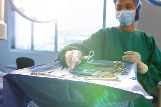Young scrub nurse selecting forceps at sterile blue draped table in operating room, copy space