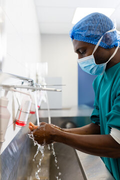 African American male medical worker washing hands at hospital scrub sink, using soap dispensers